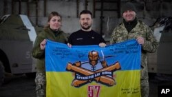 El presidente ucraniano Volodymyr Zelenskyy, en el centro, y los soldados ucranianos sostienen la bandera de una unidad militar en una posición cerca de Bakhmut, región de Donetsk, Ucrania. 