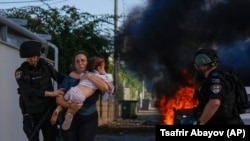 Agentes de policía evacuan a una mujer y un niño de un lugar alcanzado por un cohete disparado desde la Franja de Gaza, en Ashkelon, sur de Israel, el sábado 7 de octubre de 2023. (AP/Tsafrir Abayov)