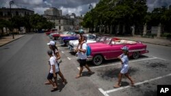 Turistas pasan frente a un estacionamiento lleno de autos clásicos estadounidenses que esperan a los clientes, en La Habana, Cuba, el 9 de julio de 2022. (Foto AP/Ramón Espinosa)