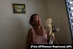 Miriam Cortés posa con su ventilador junto a una foto de Fidel Castro durante un apagón matutino programado, en su casa de Regla, Cuba, el lunes 1 de agosto de 2022.