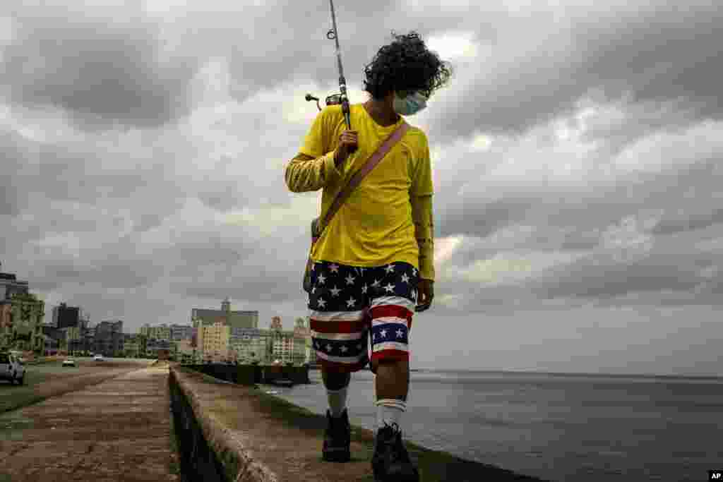 En vísperas de un toque de queda un pescador utiliza una máscara como precaución contra el contagio del nuevo coronavirus mientras camina por el muro del Malecón habanero.