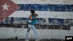 Una cubana camina ante un mural con la bandera cubana en La Habana. Foto Archivo (YAMIL LAGE / AFP)