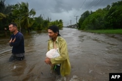 Dos hombres caminan por una calle inundada tras el paso del huracán Helene en Guanimar, provincia de Artemisa, Cuba, el 25 de septiembre de 2024. (Foto de YAMIL LAGE / AFP)