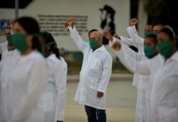 Médicos cubanos alzan sus puños en ceremonia de despedida antes de su partida a Andorra, en marzo pasado. (Yamil Lage/AFP)