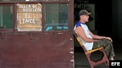 Un hombre permanece sentado en la puerta de un taller de reparación de bicicletas en La Habana