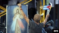 Una mujer cubana copn una imagen de Cristo y la bandera de su país en la Plaza de la Revolución de La Habana, donde el Papa oficiará su primera misa en Cuba, a la que asistirán miles personas que ya están congregadas en el que se considera uno de los luga