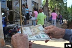 Un hombre muestra un peso convertible cubano y un dólar estadounidense frente a una oficina de la Western Union en La Habana.