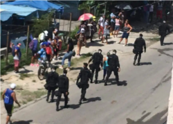 Boinas negras caminan junto a personas que permanecen en una cola.