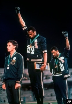 Octubre 16, 1968. John Carlos (derecha) y Tommie Smith (centro) con puños negros, y descalzos. Peter Norman con un escudo en el pecho en apoyo a ambos (AP).