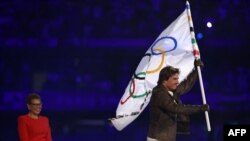 El actor Tom Cruise sale con la bandera olímpica frente a la alcaldesa de Los Ángeles, durante la ceremonia de clausura de los Juegos Olímpicos de París 2024. (Foto de Franck FIFE / AFP)