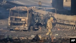 Un soldado ucraniano se desplaza entre los restos de un camión militar incendiado en una calle en Kiev, Ucrania, el sábado 26 de febrero de 2022. (AP Foto/Efrem Lukatsky)