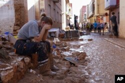 Una mujer descansa mientras residentes y voluntarios limpian una zona afectada por las inundaciones en Paiporta, cerca de Valencia, España, viernes 1 de noviembre de 2024. (AP Photo/Alberto Saiz)