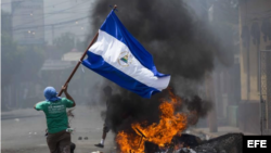 Un joven corre con la bandera de Nicaragua frente a unas llantas incendiadas ayer en la ciudad de Masaya (Nicaragua). EFE