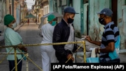 Un residente muestra su identificación a un oficial de policía que está limitando el acceso a un vecindario en La Habana. (AP Foto/Ramon Espinosa)